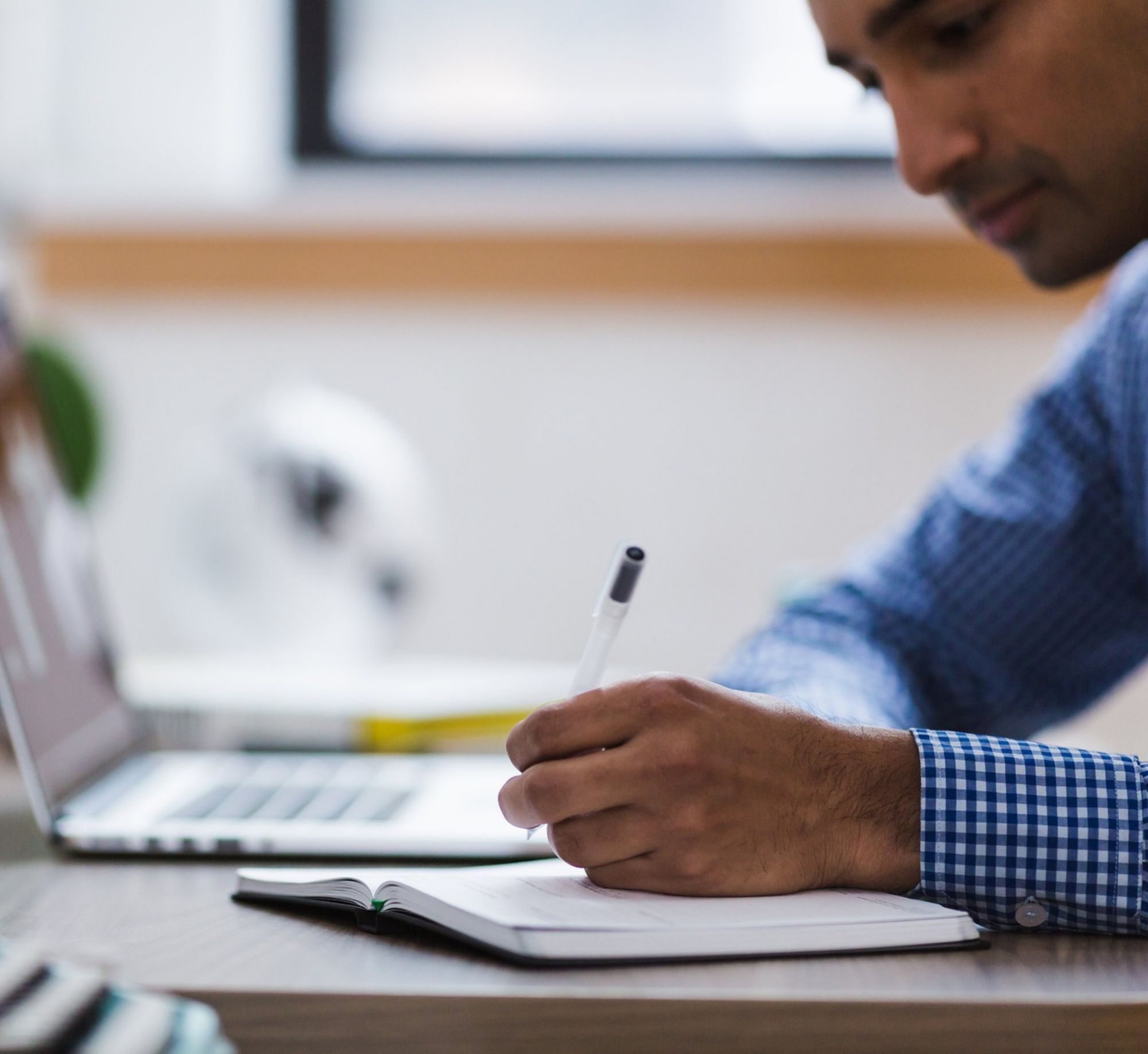 man behing laptop screen taking notes 